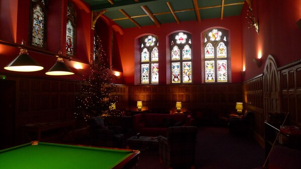 Una sala de billar con mesa de pool verde, un árbol de Navidad y vidrieras.