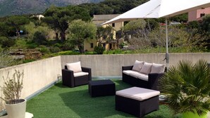 Un patio al aire libre con mobiliario de mimbre, un paraguas blanco y vistas del paisaje circundante.