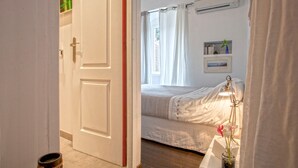 Un dormitorio con cama, aire acondicionado, mesita de noche con lámpara y ventana con cortinas.