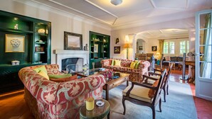 A traditional living room with a fireplace, green-painted shelves, and a dining area with wooden furniture.