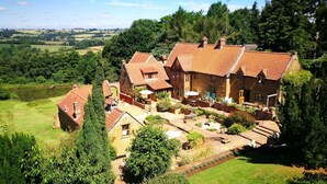 Une grande maison en pierre, dotée de nombreuses cheminées, entourée d’une végétation luxuriante et d’un jardin bien entretenu.