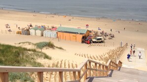 A beach with a wooden walkway leading to a sandy area with beach huts and a flag. - Gorgeous canal house in The Hague city (Den Haag)