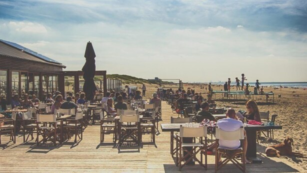 A beachside restaurant with outdoor seating on a wooden deck, overlooking the beach and ocean. - Gorgeous canal house in The Hague city (Den Haag)