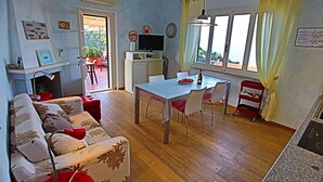 Una sala de estar con sofá, una mesa de comedor y televisor. Hay una ventana con cortinas y vista al exterior.