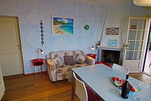 Ett vardagsrum med en soffa, ett matbord med en vinflaska och en tavla på väggen.