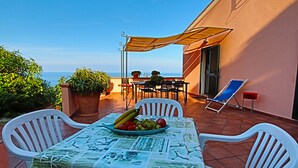 Una terraza con una mesa para dos, una silla, una sombrilla y vista al mar.
