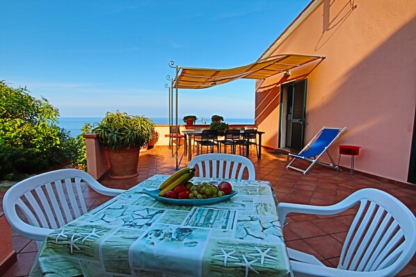 Una terraza con una mesa preparada para dos, una silla y una sombrilla.