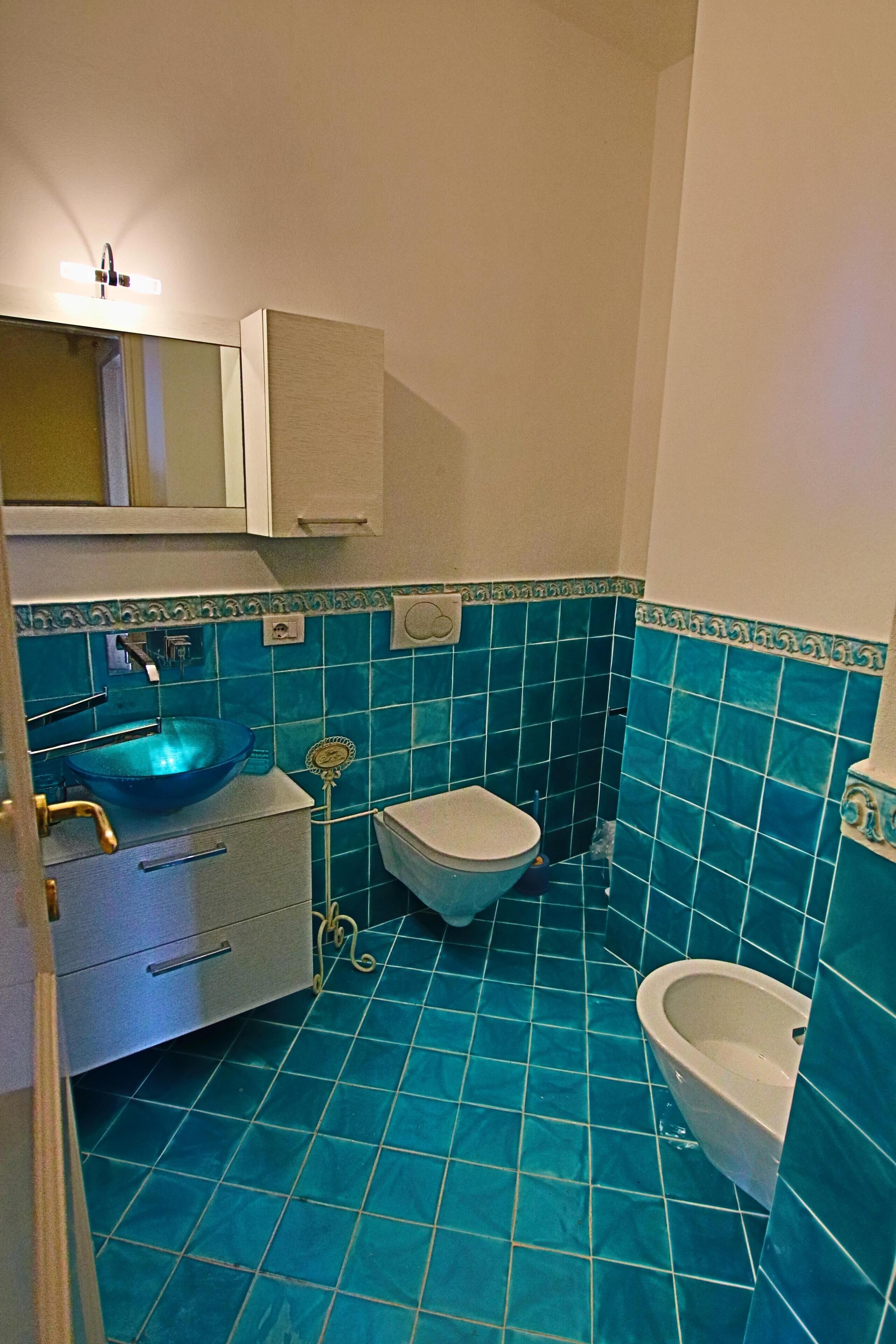 A bathroom with a blue tiled floor, a sink, a toilet, and a bidet.