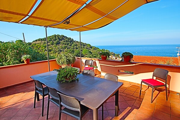 Una terraza con mesa y sillas, plantas en macetas y vista al mar.