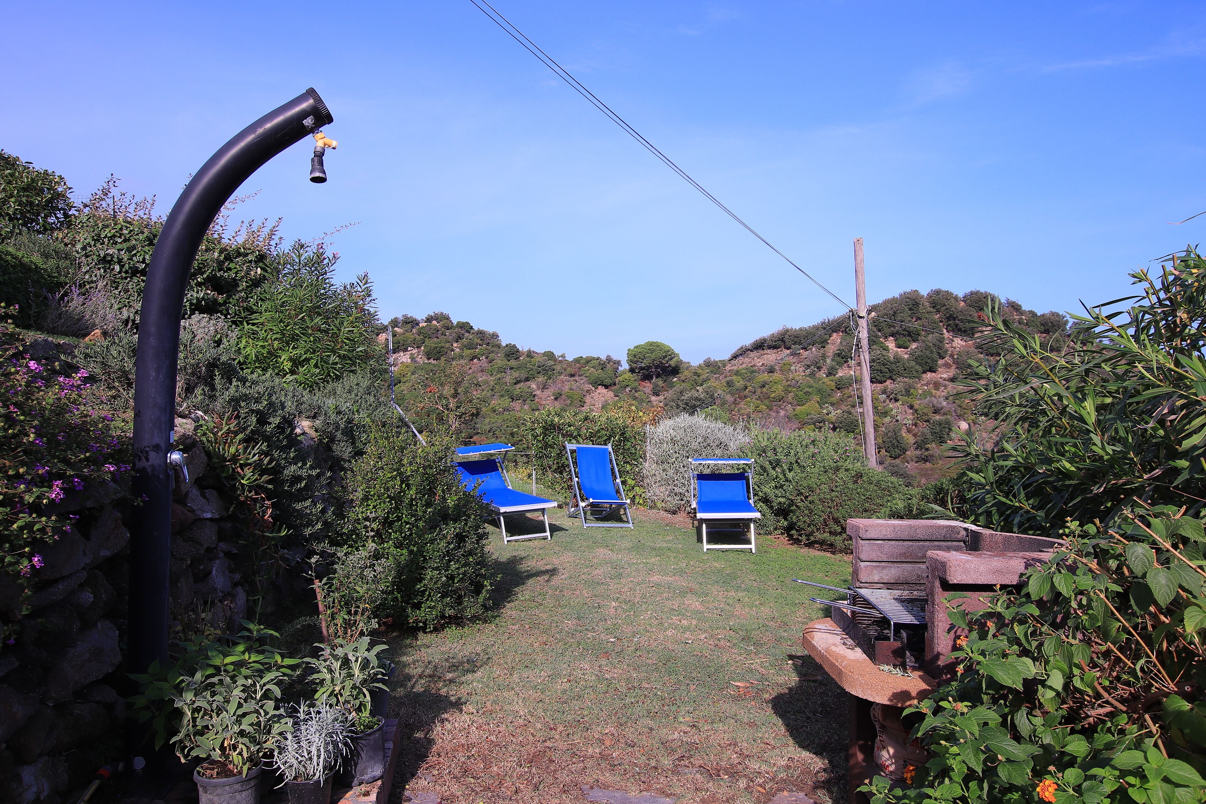 A garden with a stone wall, a metal pipe, and three blue lounge chairs.