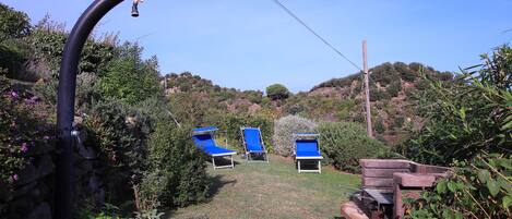 A garden with a stone wall, a metal pipe, and three blue lounge chairs.