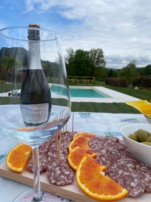 Una mesa con una botella de Prosecco, una copa de vino y una tabla de salami en rodajas con rodajas de naranja.