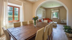 Een eetruimte met een houten tafel, beige stoelen, een vaas met bloemen en uitzicht op groen buiten.