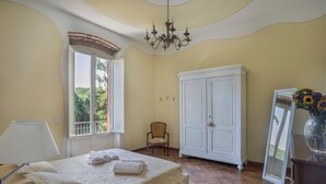 Een slaapkamer met een bed, een stoel, een kledingkast en een raam met uitzicht op groen.