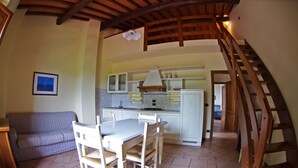 Uma área de refeições com mesa e cadeiras, uma cozinha ao fundo e uma escada.