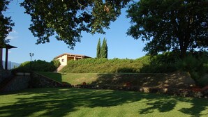 Uma área gramada bem cuidada, com um muro de pedra e um edifício com telhado em azulejos.