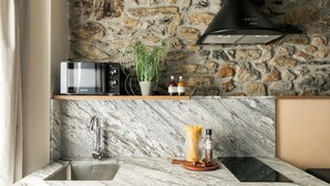 A kitchen with a stone wall, a built-in microwave, a sink, and a wooden shelf with a plant and bottles. - Enjoy our cozy 40m² diaphanous loft. Comfort and relaxation. (Aia)