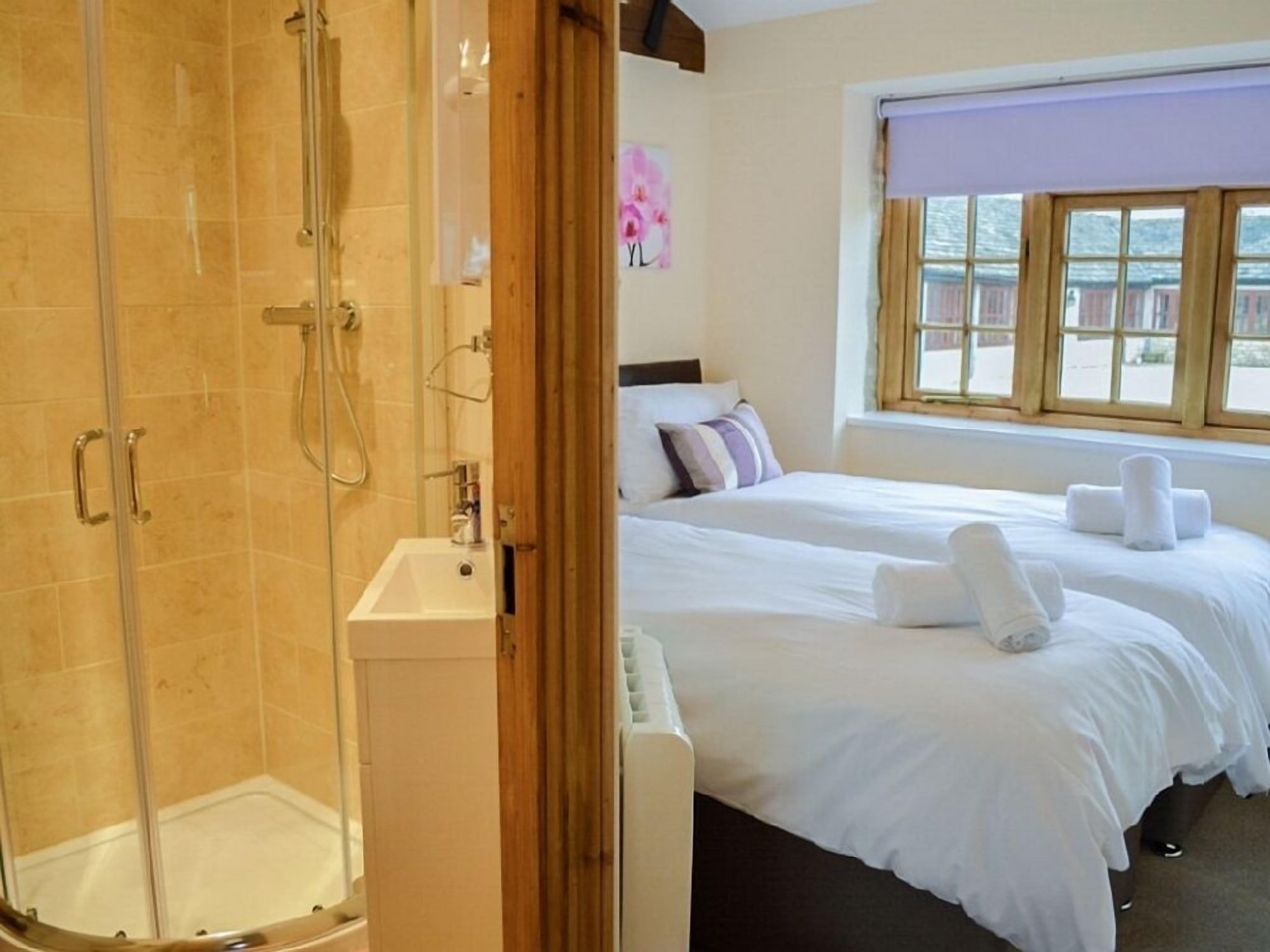 Een hotelkamer met een douchecabine van glas, een bed met witte lakens en een raam met uitzicht op gebouwen.