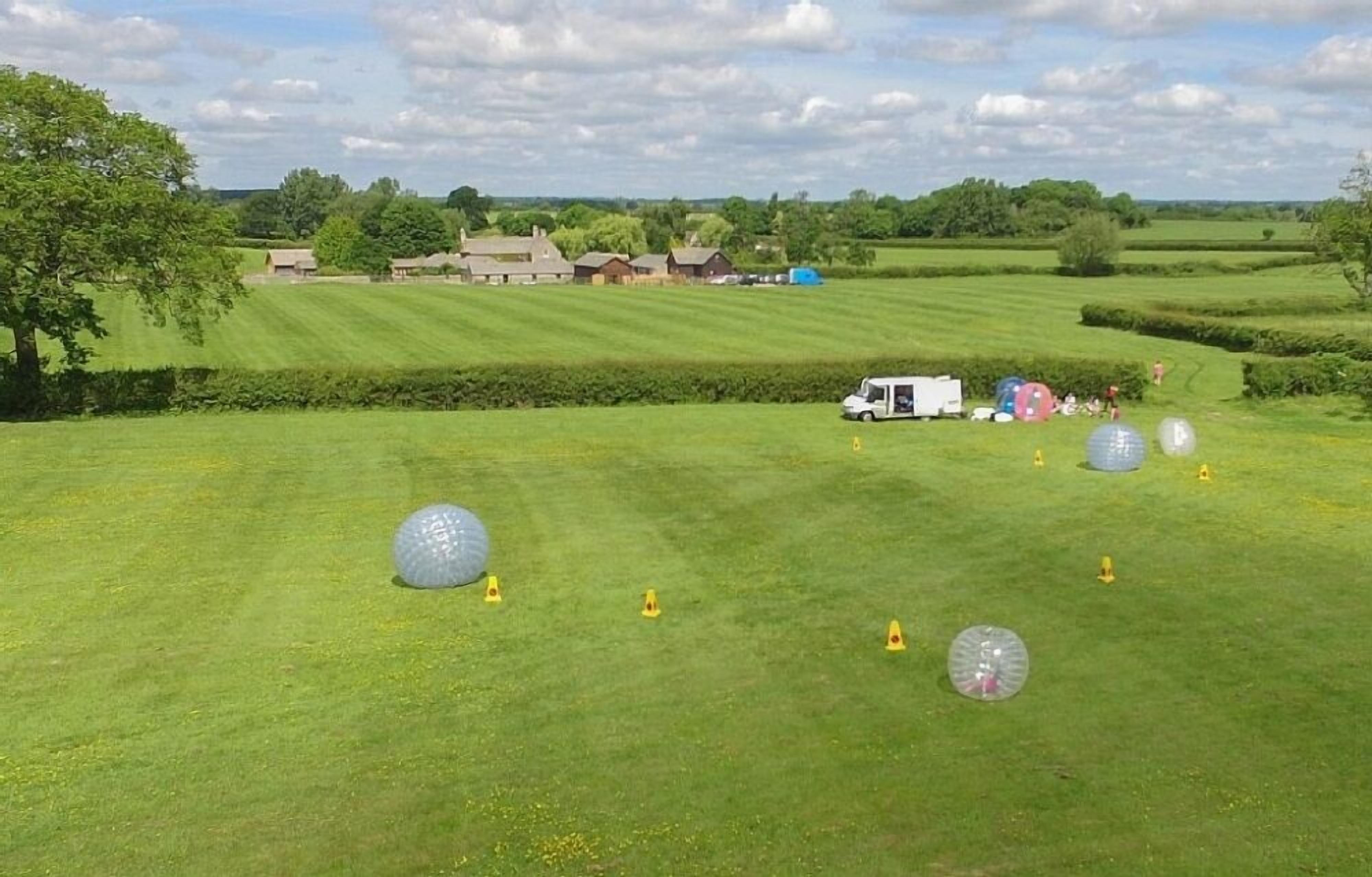 Un champ herbeux avec de grandes boules transparentes et des cônes jaunes, probablement utilisé pour une activité de loisirs.