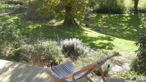 Una silla hamaca sobre una terraza de madera con vistas a un área con césped, árboles y arbustos.