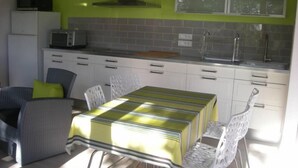 Una cocina compacta con armarios blancos, microondas y lavamanos. Hay una mesa de comedor con sillas y mantel a rayas verdes.