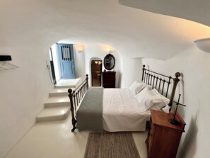 Un dormitorio con una cama, una mesita de noche de madera, un espejo y una escalera que lleva a un baño.
