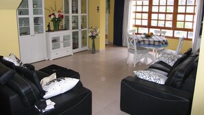 A living room with black leather sofas, a dining table with chairs, a white cabinet with glass doors, and a window with curtains. - ATICO PUERTO DE TAZACORTE (Tenerife)