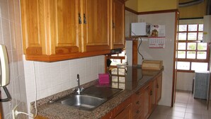 A kitchen with wooden cabinets, a granite countertop, a stainless steel sink, and a microwave. - ATICO PUERTO DE TAZACORTE (Tenerife)