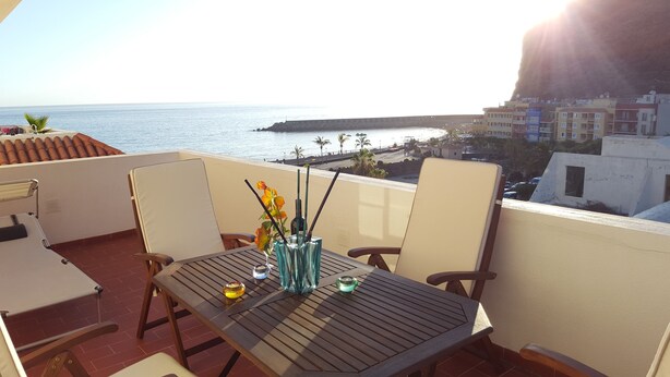 A balcony with a wooden table, chairs, and a vase with flowers. - ATICO PUERTO DE TAZACORTE (Tenerife)