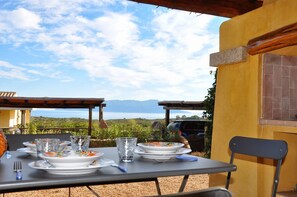 An outdoor dining area with a table set for two, overlooking a scenic landscape with mountains and a body of water.