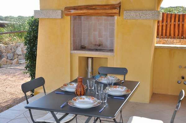 An outdoor dining area with a table set for four, a stone wall, and a view of the countryside.