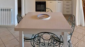 Ett kompakt kök med vita skåp, en spis och ett handfat. I förgrunden står ett matbord med stolar.