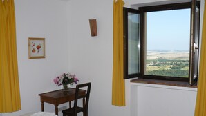 Ein Zimmer mit zwei Betten, einem Tisch mit Blumenvase, einem Fenster mit Blick und gelben Vorhängen.