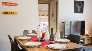 Un coin repas avec une table en bois dressée pour six personnes, un téléviseur et un panneau indiquant la présence d’une écurie.