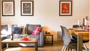 Un salon moderne avec un canapé, une table basse et un coin repas comprenant une table et des chaises. Des tableaux encadrés ornent le mur.