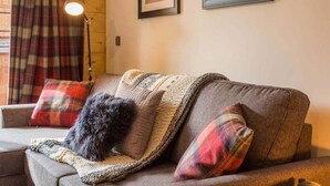 Un salon chaleureux avec un canapé, des coussins à motifs, un plaid tricoté et une lampe sur pied.