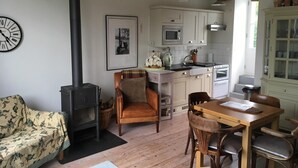 Ein gemütliches Wohnzimmer mit Kamin, ein Essbereich mit Holztisch und -stühlen sowie eine Küche mit weißen Schränken und modernen Geräten.