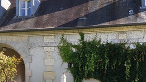 Ein Steingebäude mit überdachter Terrasse, Sitzgelegenheiten im Freien und einem Garten mit rosa Blumen.