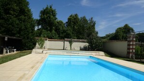 Ein rechteckiger Pool mit gefliestem Sonnendeck, umgeben von einer niedrigen Mauer und einem Zaun.