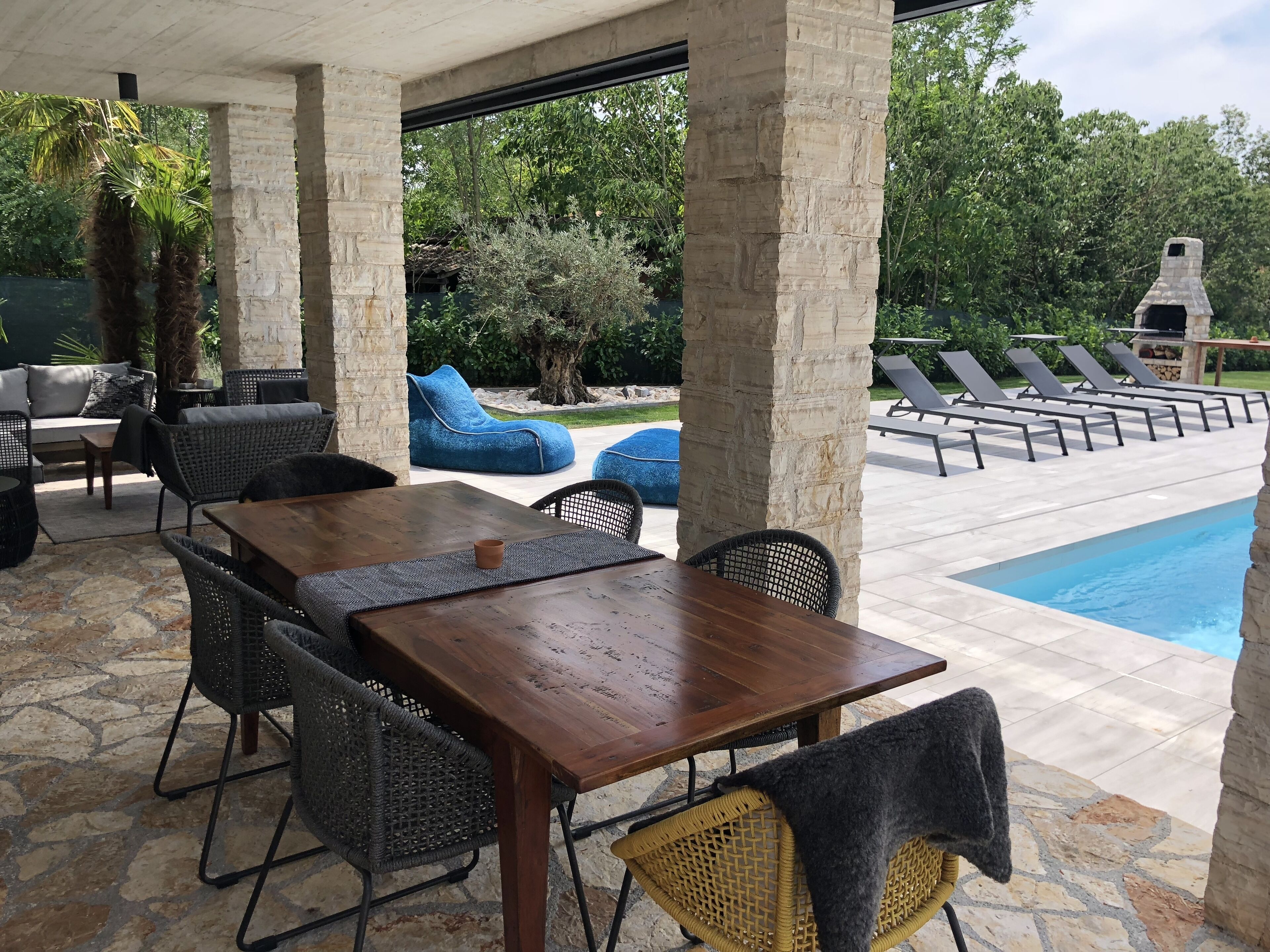Ein Patio im Freien mit Steinboden, einem Holztisch, Korbstühlen und einem Pool.