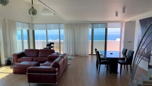 Una sala de estar moderna con un sofá de cuero, una mesa de comedor con sillas y grandes ventanales con vista al mar.