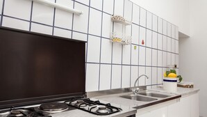 Una cocina con estufa a gas, un lavamanos y paredes cubiertas de baldosas blancas.