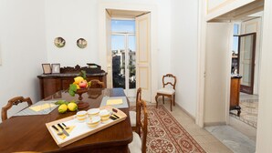 Un comedor con una mesa de madera dispuesta para cuatro personas, un frutero y vistas de la ciudad a través de un ventanal de vidrio.