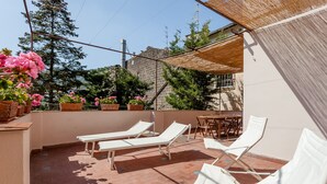 Una terraza en la azotea con sillones blancos, una mesa y plantas en macetas.