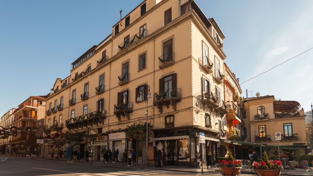 Un edificio de varios pisos con balcones, locales comerciales y un paso de peatones.