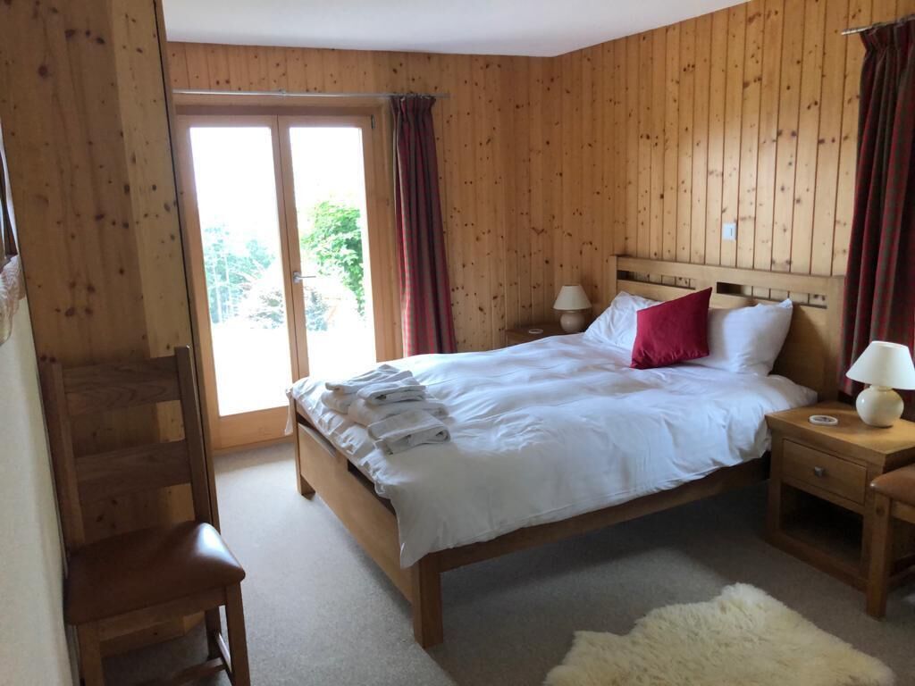 A wooden-paneled bedroom with a bed, two bedside tables, a chair, and a large window with curtains.