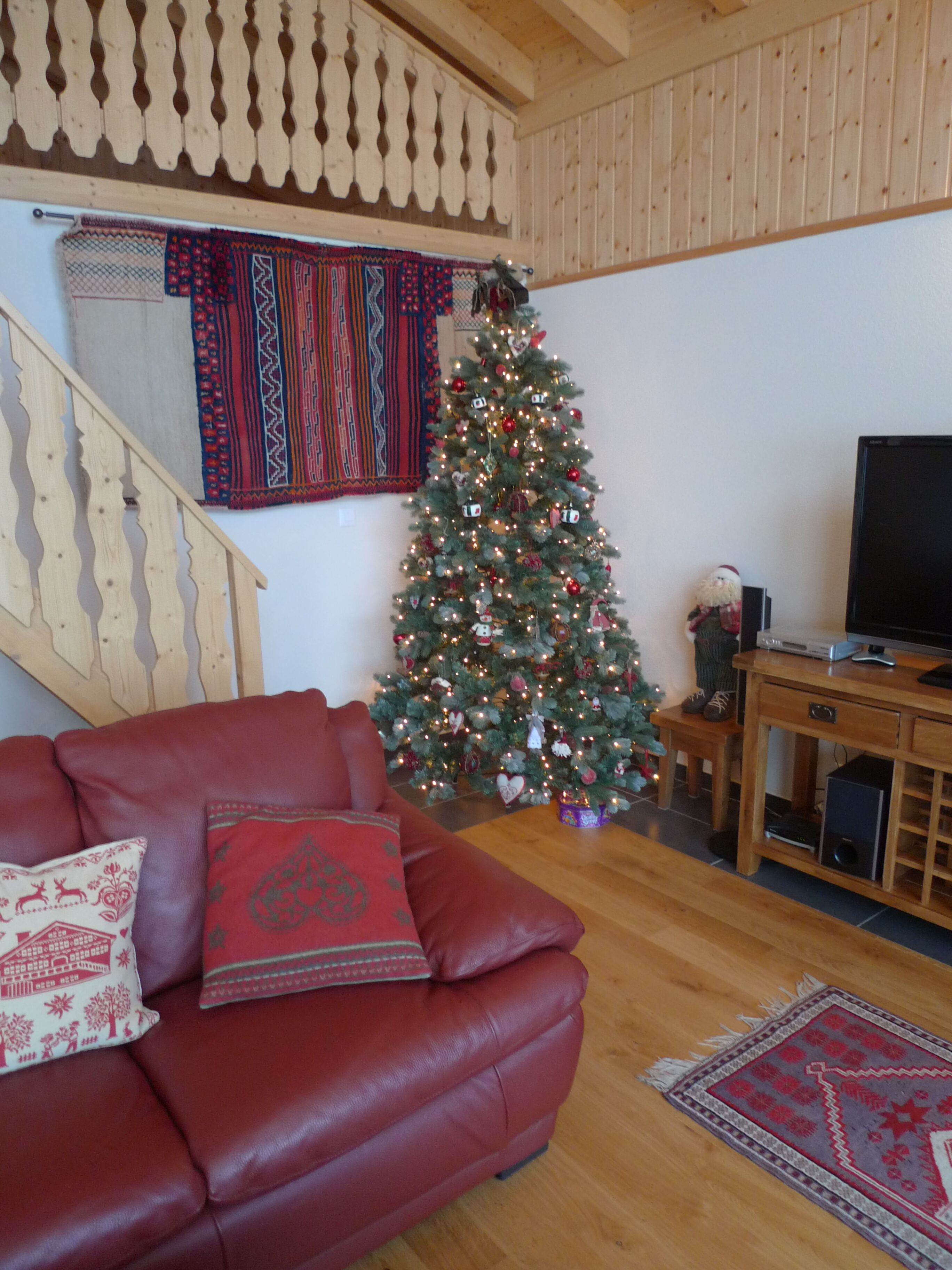 A living room with a red leather sofa, a wooden coffee table, a Christmas tree, and a television on a wooden stand.