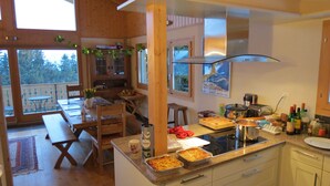 A kitchen with wooden cabinets, a central island with a stove, and a dining area with a bench and table. - Luxury Modern Swiss Chalet - Spectacular Panoramic Views - 200m From Piste (Gryon)
