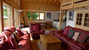 A spacious living room with red leather sofas, a wooden coffee table, and a large window providing natural light. - Luxury Modern Swiss Chalet - Spectacular Panoramic Views - 200m From Piste (Gryon)