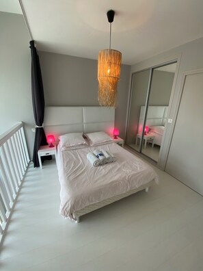 Una cama bien hecha con toallas enrolladas, una lámpara de noche y una lámpara colgante en una habitación de hotel moderna.